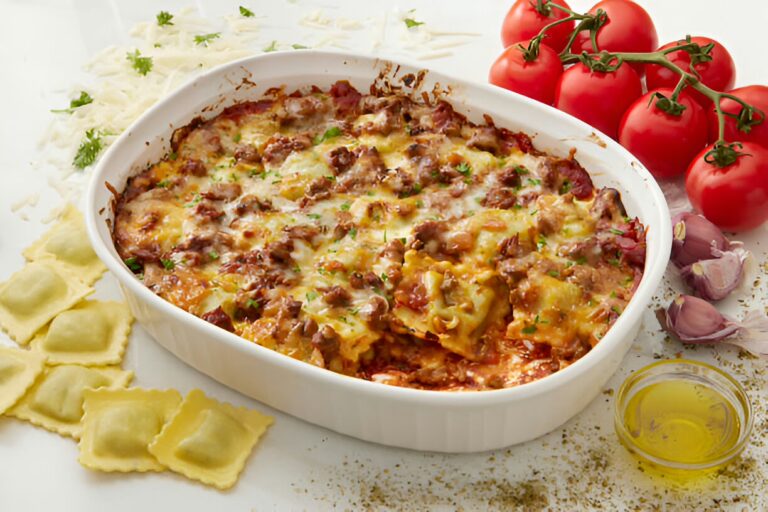 A delicious baked ravioli dish topped with melted cheese and garnished with herbs, surrounded by fresh tomatoes and garlic.