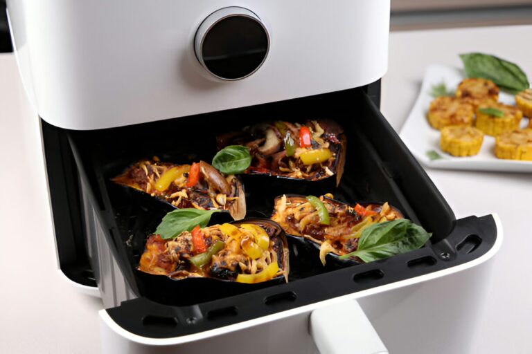 Air fryer with cooked vegetable dishes inside, including eggplant and peppers, with a side of cornbread bites.