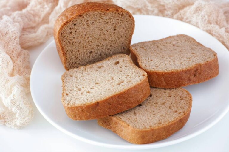 Sliced whole grain bread on a white plate with a beige cloth in the background.