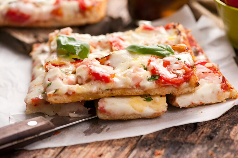 Delicious sliced pizza topped with cheese, fresh basil, and vegetables on a wooden board.
