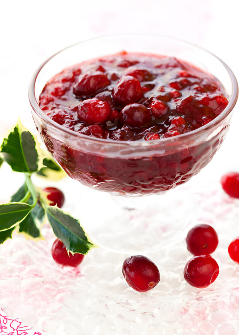 A glass bowl filled with cranberry sauce garnished with fresh cranberries and a sprig of green leaves.