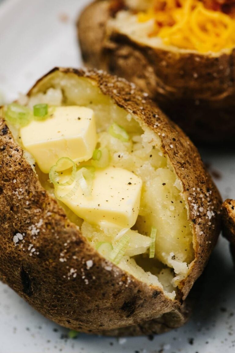 A baked potato halved, filled with butter and chopped green onions, sitting on a plate.