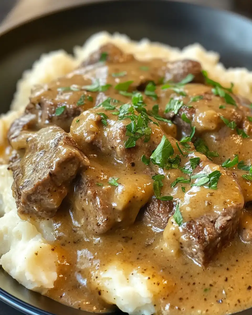 Serving plate of cubed steak with thick gravy, mashed potatoes, and herbs